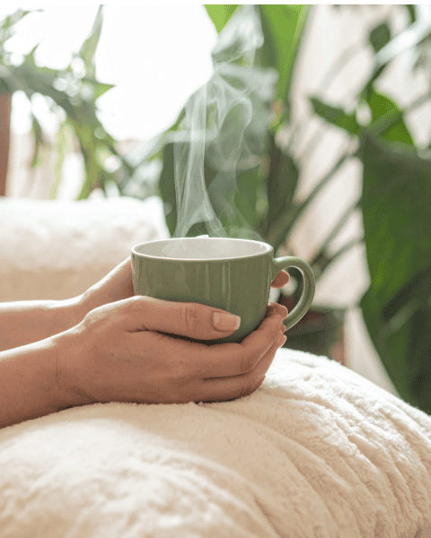 Hand holding a steaming green mug surrounded by plants, representing calm, mindfulness, and choosing which balls to catch.
