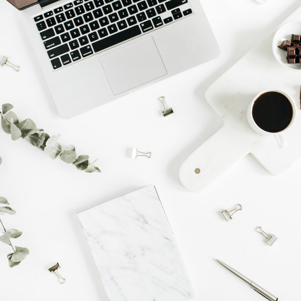 Image of a laptop on a desk with coffee cup, bulldog clips and a notebook