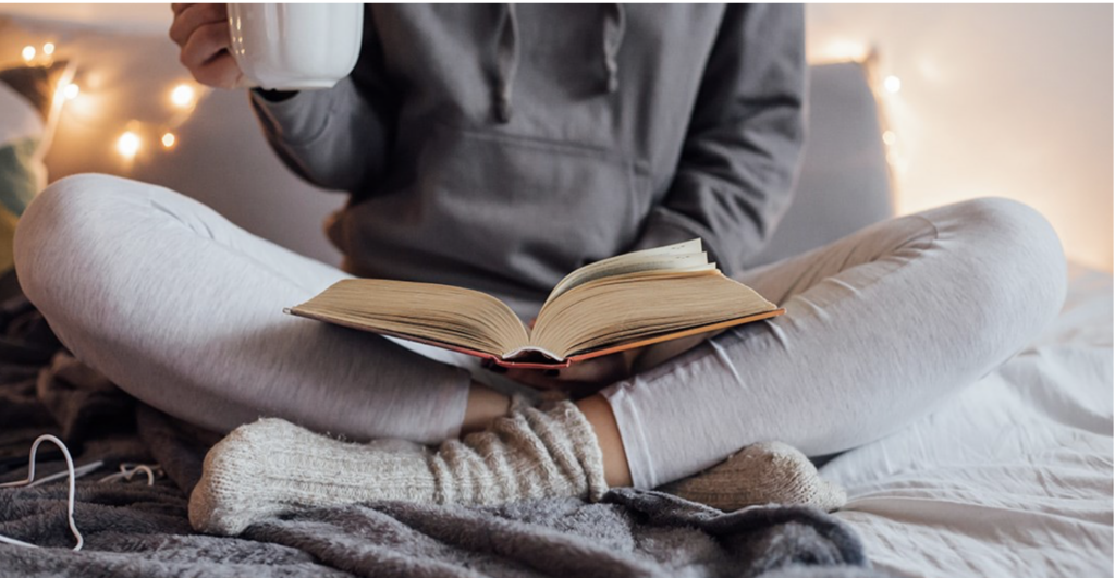 woman sitting cross legged with a book and a drinking from a mug